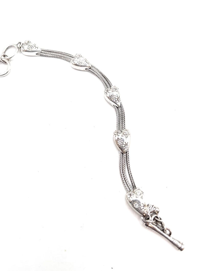 May include: A silver watch chain with a heart-shaped design. The chain has a decorative floral pattern and a key ring.