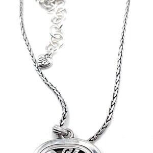 May include: Silver-toned necklace featuring a square pendant with an openwork design of swirling patterns. The chain is a braided style, and the necklace has an adjustable length.