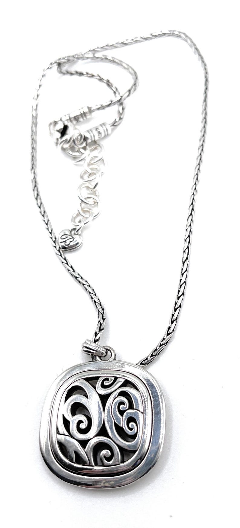 May include: Silver-toned necklace featuring a square pendant with an openwork design of swirling patterns. The chain is a braided style, and the necklace has an adjustable length.