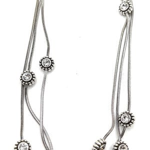 Może przedstawiać: Srebrny naszyjnik z trzema sznurami. Każdy sznur ma przezroczyste, okrągłe kamienie szlachetne osadzone w ramie w kształcie kwiatu. Naszyjnik ma delikatny, elegancki design, odpowiedni na r&oacute;żne okazje.