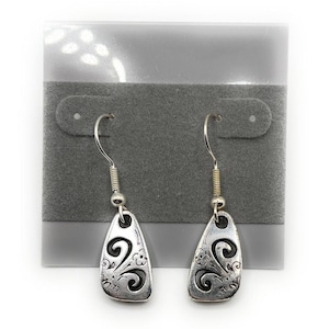 Może przedstawiać: Para srebrnych kolczyków w kształcie łezki. Każdy kolczyk ma dekoracyjny kwiatowy wzór i haczyk do przekłutych uszu. Kolczyki są prezentowane na szarej karcie do kolczyków.