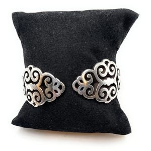 May include: A silver bracelet with a delicate, intricate design. The bracelet is on a black velvet cushion.