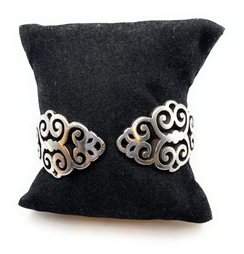 May include: A silver bracelet with a delicate, intricate design. The bracelet is on a black velvet cushion.