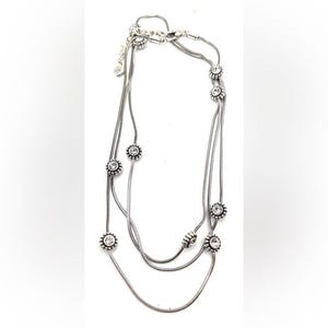 Może przedstawiać: Srebrny naszyjnik z trzema sznurami. Każdy sznur ma przezroczyste, okrągłe kamienie szlachetne w kwiatowym wzorze. Naszyjnik ma zapięcie na karabińczyk.
