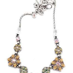 May include: Silver-toned necklace featuring a floral design. The necklace has a chain with a series of enameled flower pendants in shades of orange, green, and red, each with a central crystal. Additional crystals are set along the chain.