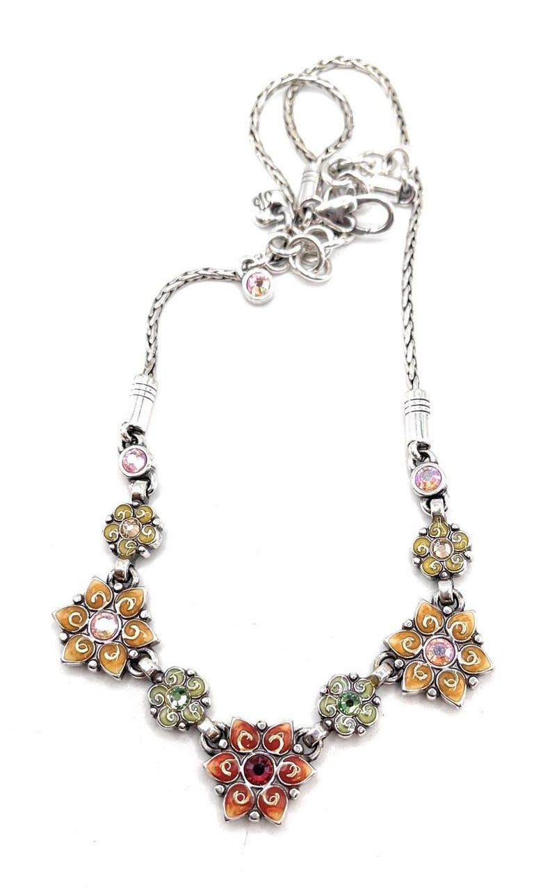 May include: Silver-toned necklace featuring a floral design. The necklace has a chain with a series of enameled flower pendants in shades of orange, green, and red, each with a central crystal. Additional crystals are set along the chain.