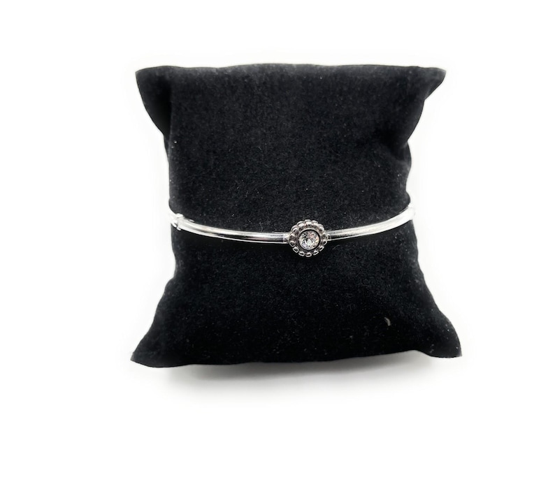 Puede incluir: Un brazalete de plata con un cristal transparente engastado en un dise&ntilde;o de flor de plata.