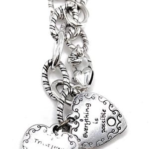 May include: Silver charm bracelet with two heart-shaped charms. One charm says "Trust your journey" and the other says "Everything is possible".