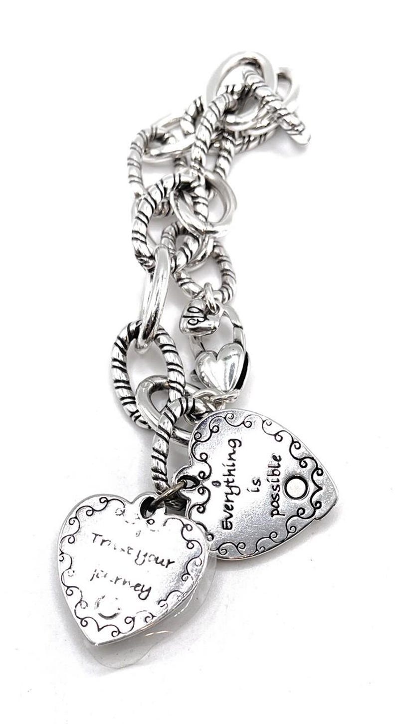 May include: Silver charm bracelet with two heart-shaped charms. One charm says "Trust your journey" and the other says "Everything is possible".