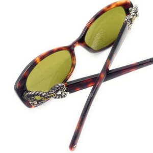Puede incluir: Gafas de sol carey con lentes verdes. Las monturas tienen un acento decorativo plateado y dorado en las patillas. Las varillas son de color marr&oacute;n oscuro.