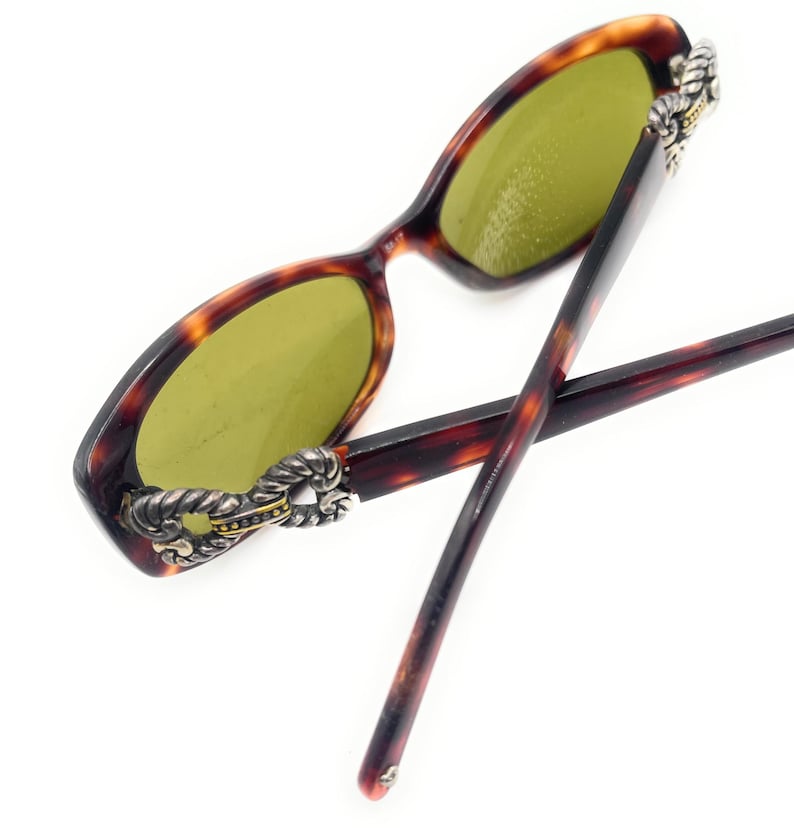 Puede incluir: Gafas de sol carey con lentes verdes. Las monturas tienen un acento decorativo plateado y dorado en las patillas. Las varillas son de color marr&oacute;n oscuro.