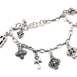 May include: A silver charm bracelet with multiple charms, including crosses, a small box with a cross inside, and a flower. The bracelet is made of a silver chain with a lobster clasp.
