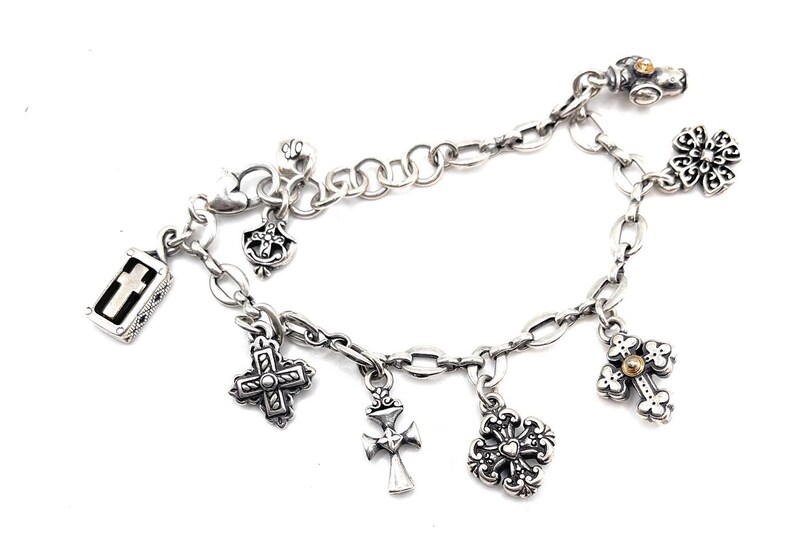May include: A silver charm bracelet with multiple charms, including crosses, a small box with a cross inside, and a flower. The bracelet is made of a silver chain with a lobster clasp.