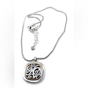 May include: Silver-tone necklace with a square pendant. The pendant has a gold-tone border and a black filigree design. The necklace chain is a woven style with an adjustable clasp. The pendant measures approximately 1 inch square.