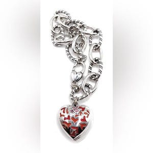 May include: Silver chain necklace with a heart-shaped pendant. The pendant is red with a filigree design and pink accents.