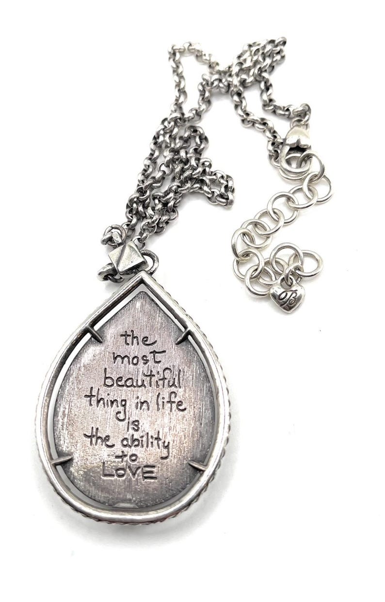 May include: Silver-toned necklace with a teardrop pendant. The pendant features the engraved quote, "the most beautiful thing in life is the ability to LOVE." The necklace has a chain with an adjustable length.