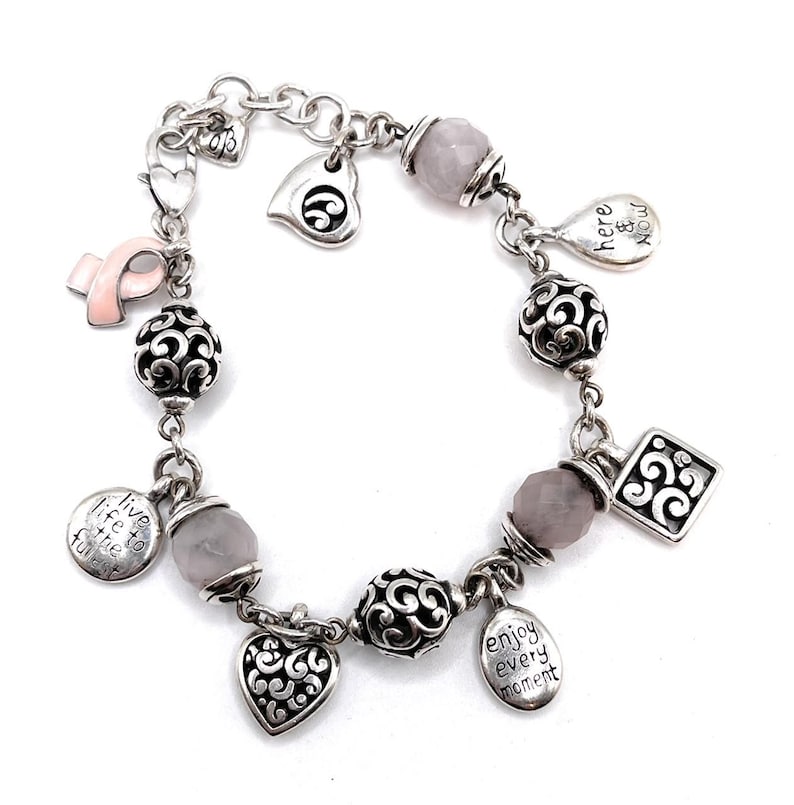 Peut inclure: Bracelet &agrave; breloques argent&eacute; avec ruban rose, c&oelig;ur et breloques rondes. Le bracelet comprend des perles grises et des breloques avec les mots "live life to the fullest" et "enjoy every moment".
