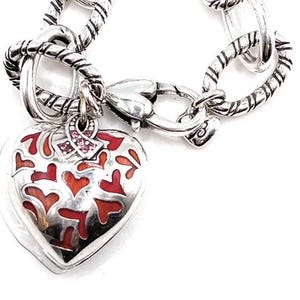 May include: Silver charm bracelet with a heart-shaped charm featuring a red and white enamel design. The charm also has a pink ribbon with small pink rhinestones.