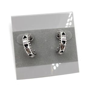 May include: A pair of silver-toned hoop earrings. Each earring has a curved design with heart-shaped cutouts and decorative detailing. The earrings are displayed on a gray earring card.