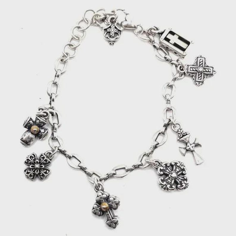 May include: A silver charm bracelet with multiple cross-shaped charms, including a small gold cross charm.