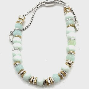 May include: A bracelet featuring alternating light mint green faceted beads and small metallic spacers in silver and gold tones. The design includes a sliding adjustable closure mechanism with a box-style chain and two small metal end caps.