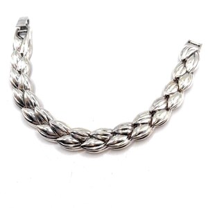May include: A silver bracelet with a braided design. The bracelet is made of a series of connected, leaf-shaped links.