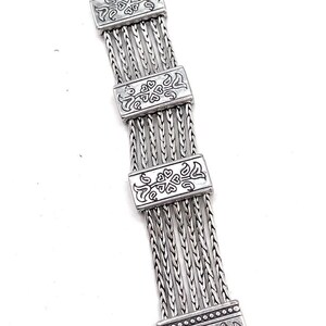 Puede incluir: Un brazalete de plata con un dise&ntilde;o de cadena de eslabones y abalorios rectangulares decorativos. Los abalorios tienen un patr&oacute;n floral.