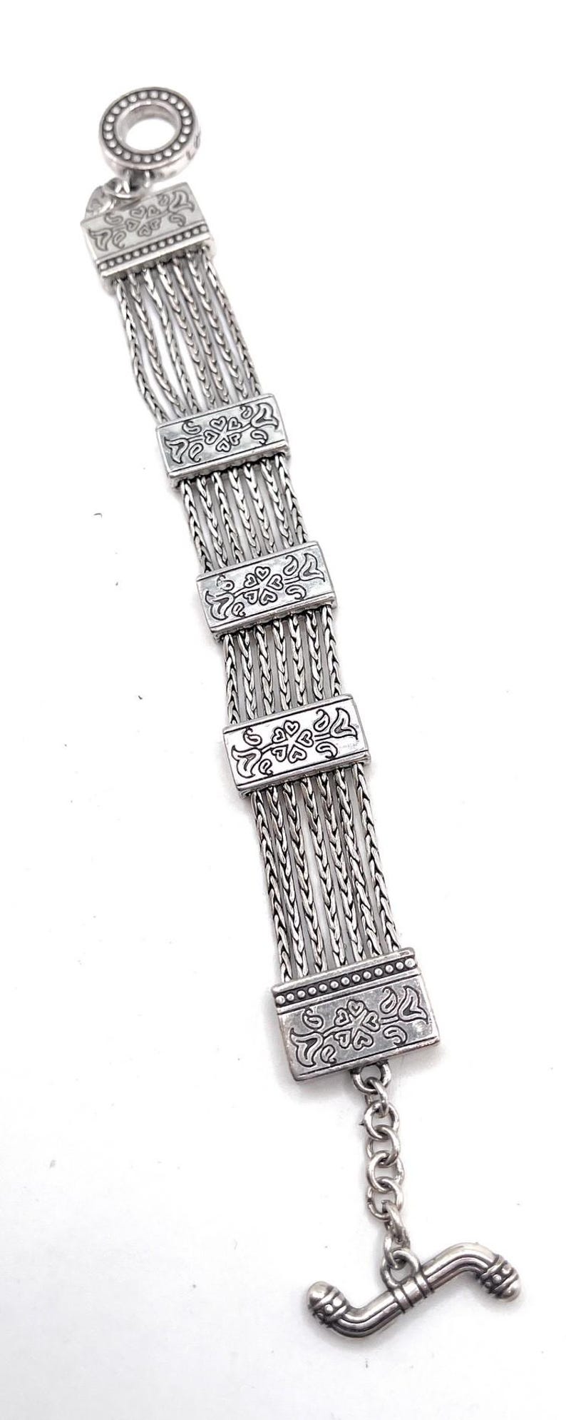 Puede incluir: Un brazalete de plata con un dise&ntilde;o de cadena de eslabones y abalorios rectangulares decorativos. Los abalorios tienen un patr&oacute;n floral.