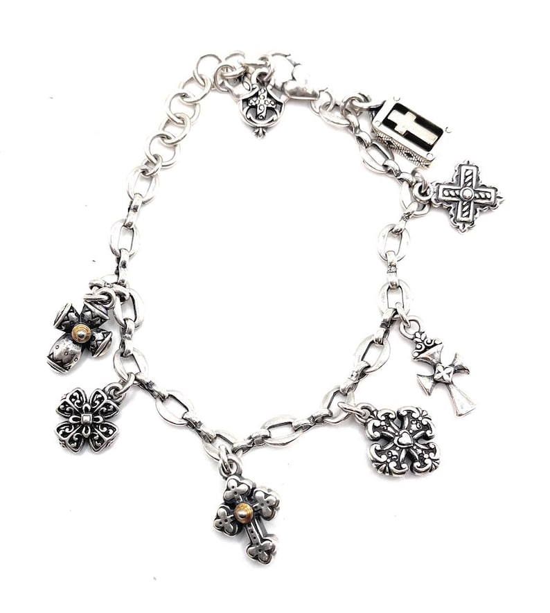 May include: A silver charm bracelet with multiple cross-shaped charms, including a small gold cross charm.