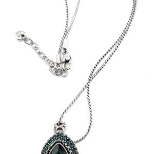 K&ouml;nnte beinhalten: Silberfarbene Halskette mit einem Anh&auml;nger, der einen gro&szlig;en, tropfenf&ouml;rmigen, dunkelgr&uuml;nen Edelstein in der Mitte hat. Der Anh&auml;nger ist von kleineren, hellgr&uuml;nen Edelsteinen umgeben. Die Kette hat ein filigranes Design und einen Karabinerverschluss.