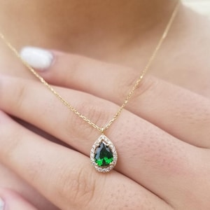 May include: A gold chain necklace with a pear-shaped green gemstone pendant surrounded by a halo of smaller clear gemstones.
