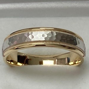 May include: A two-tone gold wedding band with a hammered finish. The band is made of both yellow and white gold.