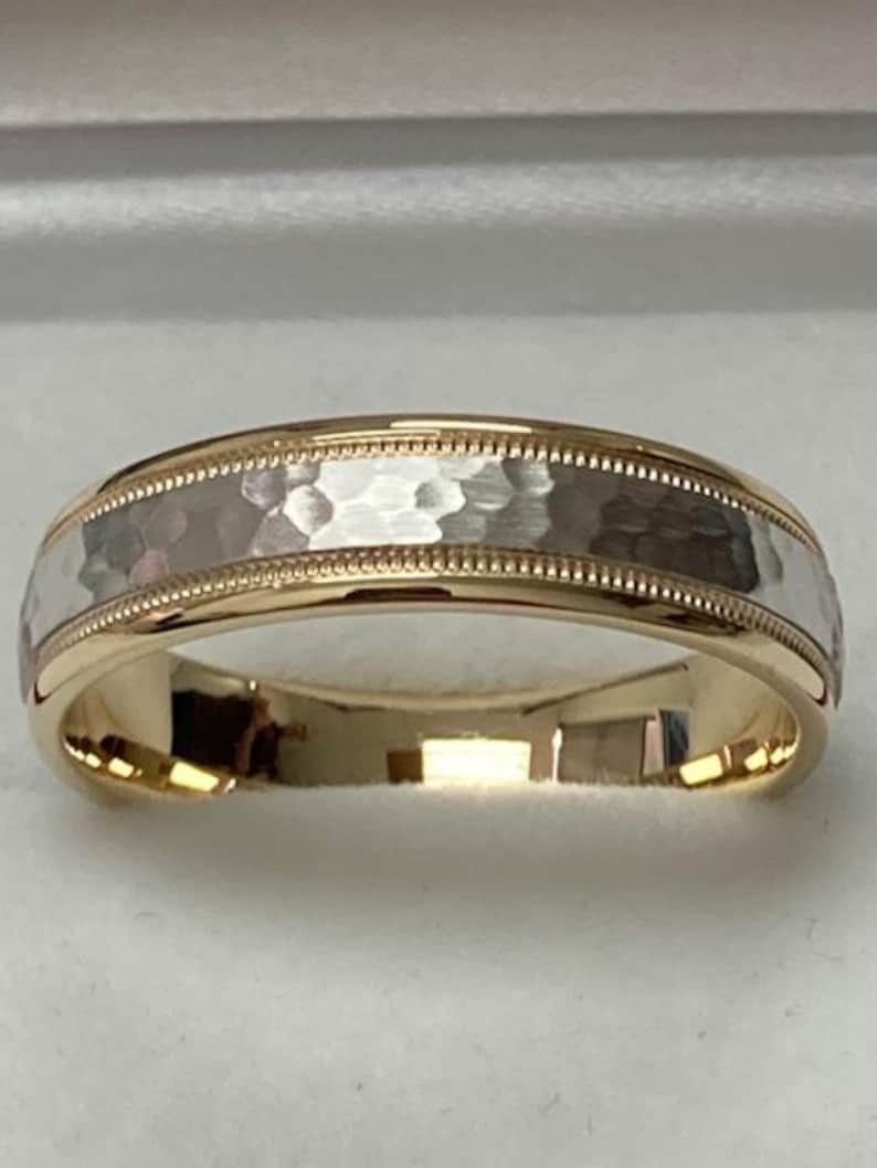 May include: A two-tone gold wedding band with a hammered finish. The band is made of both yellow and white gold.