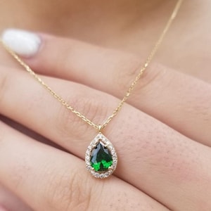 May include: A gold necklace with a pear-shaped green gemstone pendant surrounded by a halo of smaller clear gemstones.