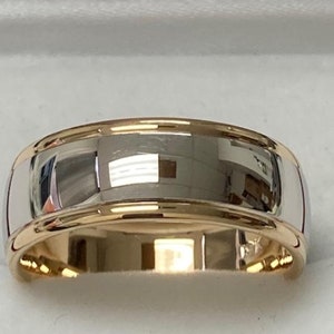 May include: A silver wedding band with a gold trim. The band is polished and has a rounded profile.