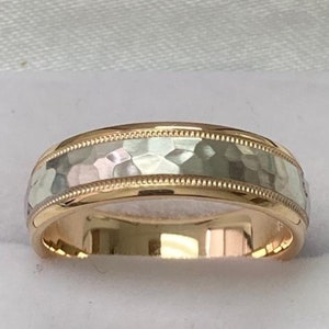 May include: A gold and silver wedding band with a hammered finish. The band has a thin, beaded edge.