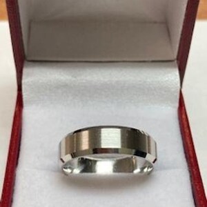 May include: A silver wedding band with a beveled edge and a brushed finish. The band is in a red velvet ring box.