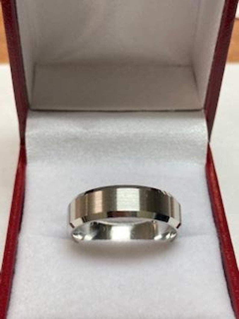 May include: A silver wedding band with a beveled edge and a brushed finish. The band is in a red velvet ring box.