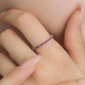 May include: A delicate eternity band ring with a row of small pink gemstones set in a silver band.