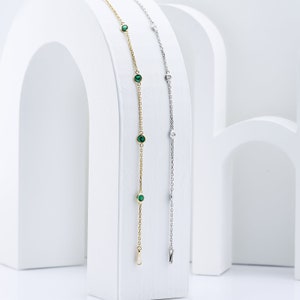 Puede incluir: Dos delicados brazaletes de cadena con peque&ntilde;as piedras preciosas verdes y transparentes. El brazalete de la izquierda es de oro y el brazalete de la derecha es de plata.