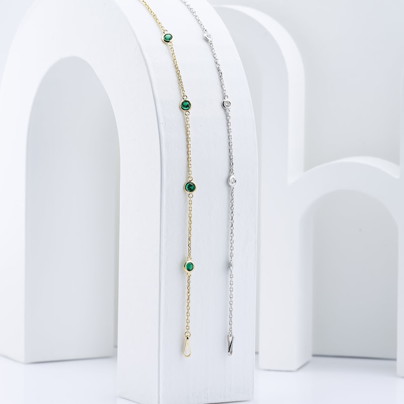 Puede incluir: Dos delicados brazaletes de cadena con peque&ntilde;as piedras preciosas verdes y transparentes. El brazalete de la izquierda es de oro y el brazalete de la derecha es de plata.