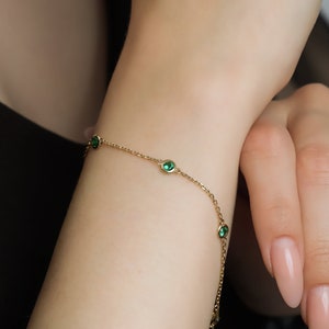 Puede incluir: Un delicado brazalete de cadena dorada con peque&ntilde;as piedras preciosas verdes. El brazalete est&aacute; en la mu&ntilde;eca de una persona.