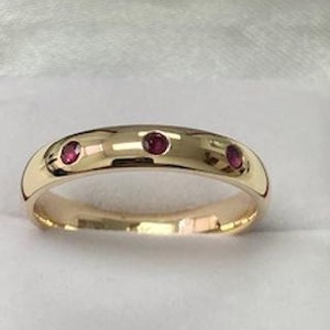 May include: A gold band ring with three small ruby red stones set in the band.
