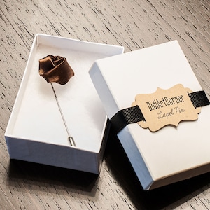 Op de afbeelding: Een bruine zijden roos revers speld in een witte doos met een bruin label met de tekst "DidiArtCorner Lapel Pin".