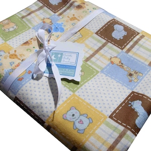 May include: A folded baby blanket featuring a patchwork pattern of squares in yellow, green, and blue with illustrations of teddy bears, giraffes, and elephants. A white ribbon is tied around the blanket with a tag labeled Cuddle Baby Boutique.