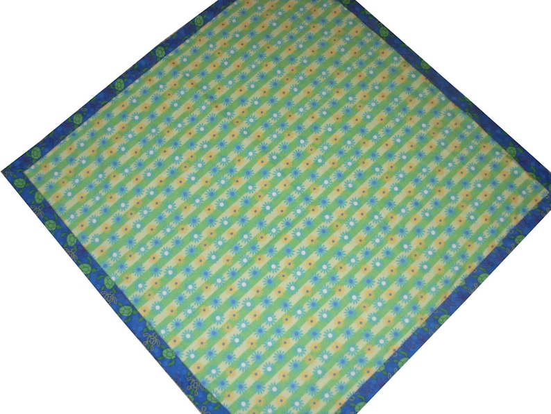 May include: A square fabric bandana featuring a diagonal pattern of alternating light green and yellow stripes. The design is accented with small blue and white flower motifs. A dark blue border frames the piece, decorated with green turtle icons.