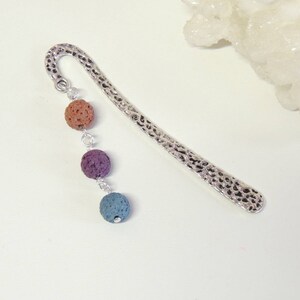 May include: Silver bookmark with a textured surface and three lava rock beads. The beads are orange, purple, and blue.