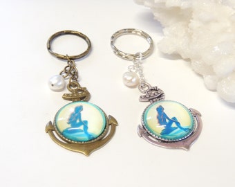May include: Two keyrings with an anchor design and a mermaid silhouette. One has a bronze finish, the other a silver finish. Each has a pearl accent and a round key ring.