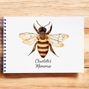 Może przedstawiać: Biały notes w spirali z akwarelową ilustracją pszczoły na okładce. Pszczoła jest brązowa i żółta w czarne paski. Tekst "Charlotte's Memories" jest napisany pod pszczołą.