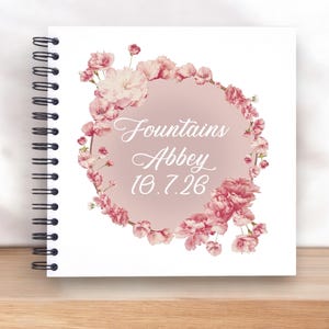 May include: A white spiral bound journal with a pink floral design and the text "Fountains Abbey 10.7.26" on the cover.